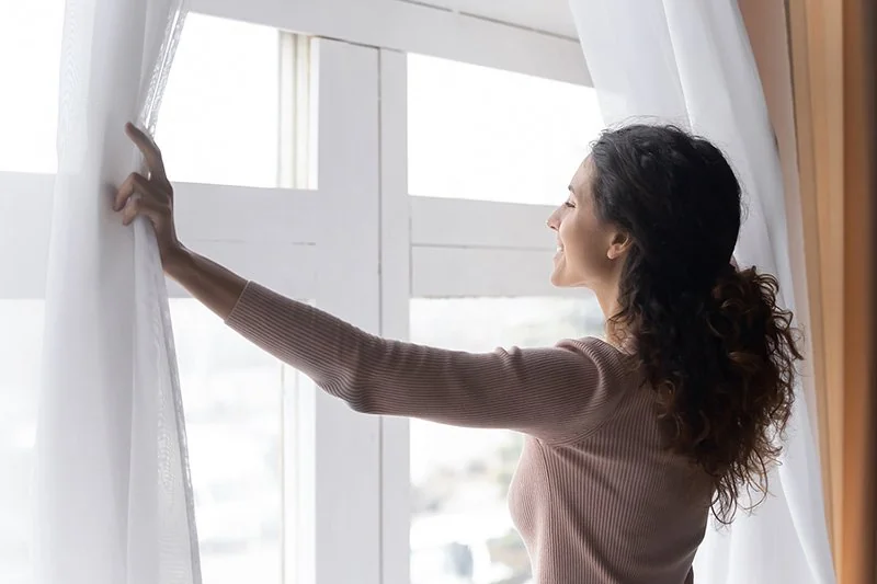 Smiling Woman Opening Curtains in Morning, Enjoying Sunlight