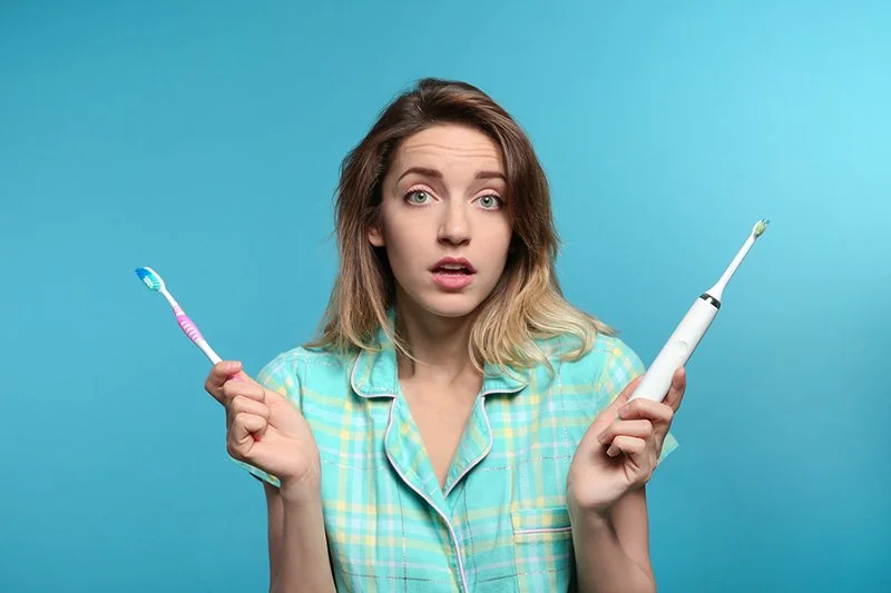 Young Woman Choosing Between Manual And Electric Toothbrushes